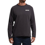 A person wears the La Sportiva Tufa Sweater Men's (2025)—a dark, long-sleeve climbing top with a small rectangular logo on the chest—paired with dark pants, standing with arms relaxed at their sides.