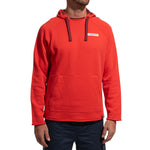 A man stands against a plain white background, wearing the La Sportiva Telendos Hoody Men's (2025) in bright red organic cotton with a front pocket, dark drawstrings, and a small rectangular logo on the left chest, paired with dark pants.