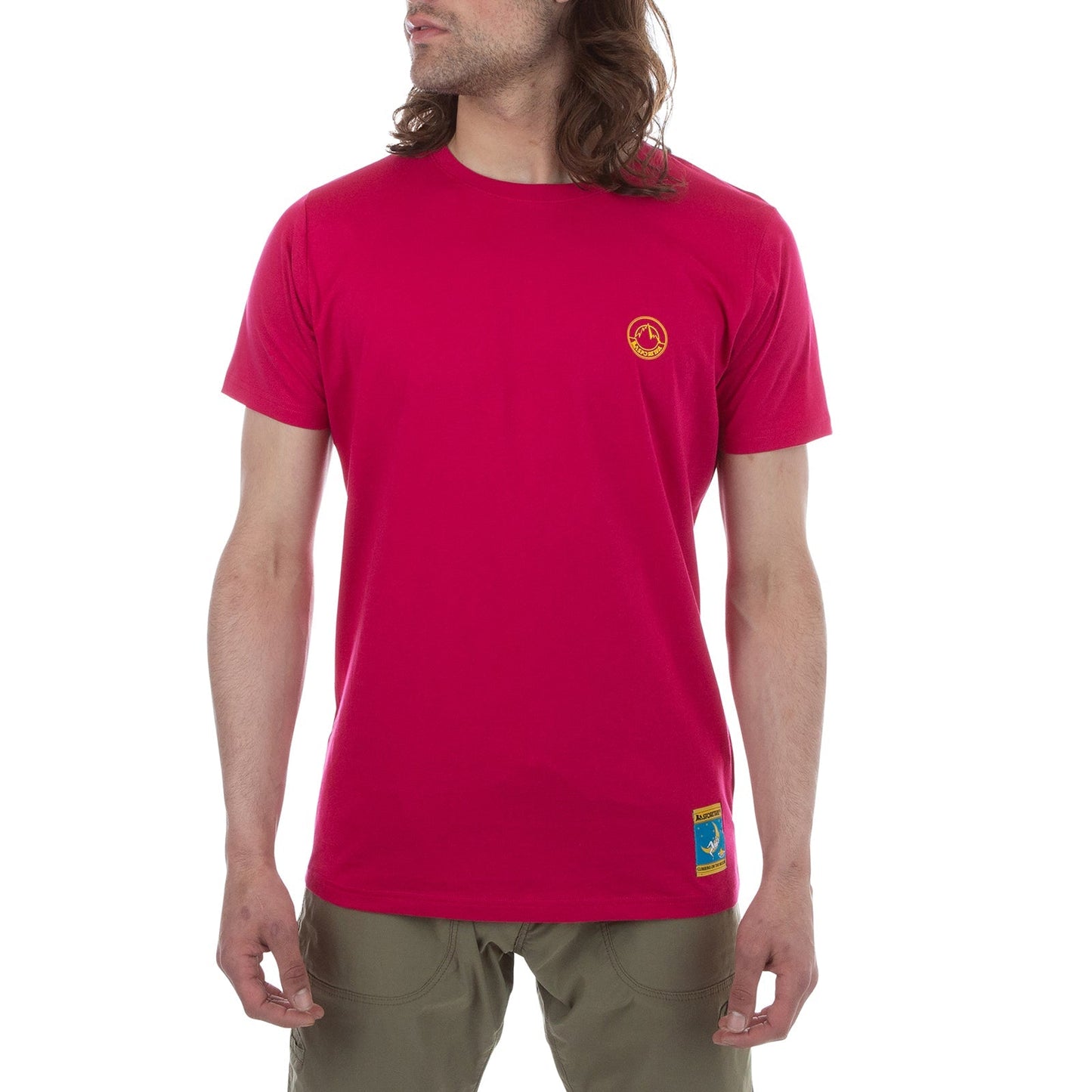 A person with long hair wears the La Sportiva Climbing On The Moon T-Shirt Men's (2025) in bright pink, featuring a small yellow logo on the left chest and blue patch near the hem, paired with olive green pants against a plain white background.