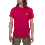 A person with long hair wears the La Sportiva Climbing On The Moon T-Shirt Men's (2025) in bright pink, featuring a small yellow logo on the left chest and blue patch near the hem, paired with olive green pants against a plain white background.