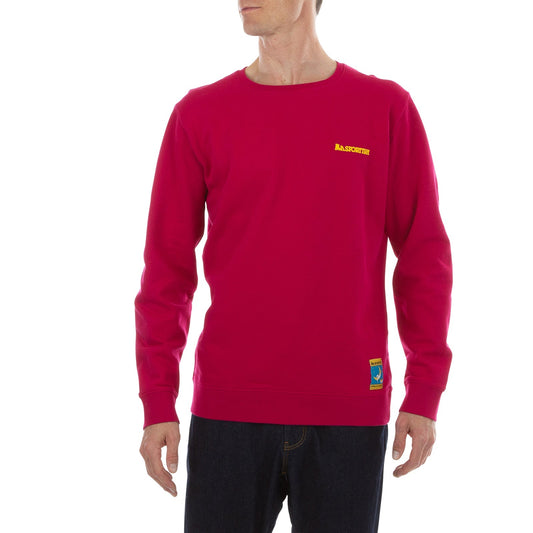 A man stands against a white background wearing the bright red La Sportiva Climbing On The Moon Sweatshirt Men's (2025), made from natural fibers, with a small yellow logo on the left chest, blue waist label, and paired with dark jeans.