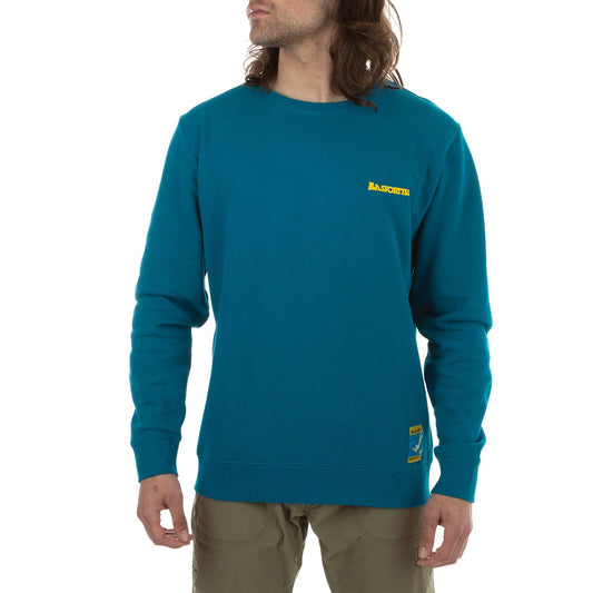 A person with long hair wears a teal La Sportiva Climbing On The Moon Sweatshirt Men's (2025) made from natural fiber, featuring a small yellow logo on the left chest and a yellow hem patch, paired with khaki pants against a white background.