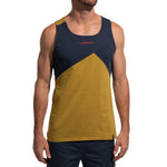 A man wears the La Sportiva Dude Tank Men's (2025), a sleeveless climbing top with navy and mustard color blocking plus a red logo on the chest, paired with dark blue shorts. His face is not visible.