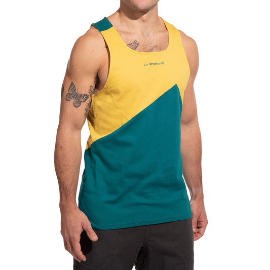 A man wears the La Sportiva Dude Tank Men's (2025), a sleeveless climbing top with diagonal yellow and teal blocks and the logo on the chest, revealing his upper arm tattoos as he stands with arms relaxed.