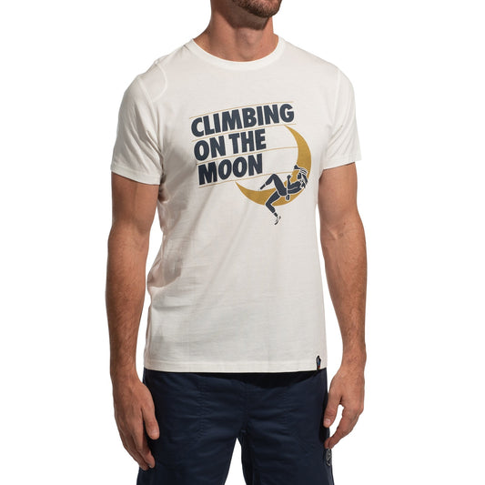 A man wears the La Sportiva Moon Rock T-Shirt Men's (2025) featuring "CLIMBING ON THE MOON" text and a graphic of a person climbing a yellow crescent moon, paired with dark blue shorts against a white background.