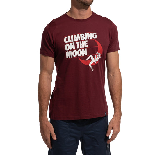 A man wears the La Sportiva Moon Rock T-Shirt Men's (2025) in maroon, made from Organic Cotton, with “CLIMBING ON THE MOON” and a climber on a crescent moon, paired with dark shorts against a white background.