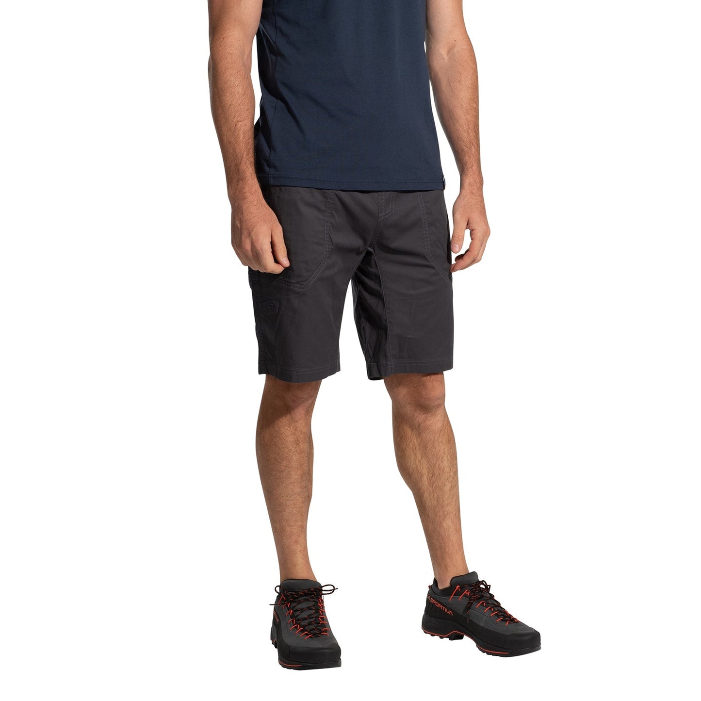 A man wearing La Sportiva Bolt Shorts Men's (2025) in navy, a matching navy t-shirt, and black hiking shoes with orange laces stands against a white background. His head is not visible in the image.