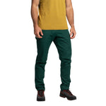 A person wearing a mustard yellow organic cotton t-shirt, La Sportiva Roots Pants Men's (2025) in dark green, and black hiking shoes with red laces, standing against a plain white background.