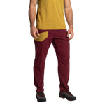 A person stands facing forward against a white background, wearing La Sportiva Labyrinth Pants Men's (2025) in maroon with a mustard pocket and adjustable waistband, a mustard yellow t-shirt, and black hiking shoes. The person's head is not visible.