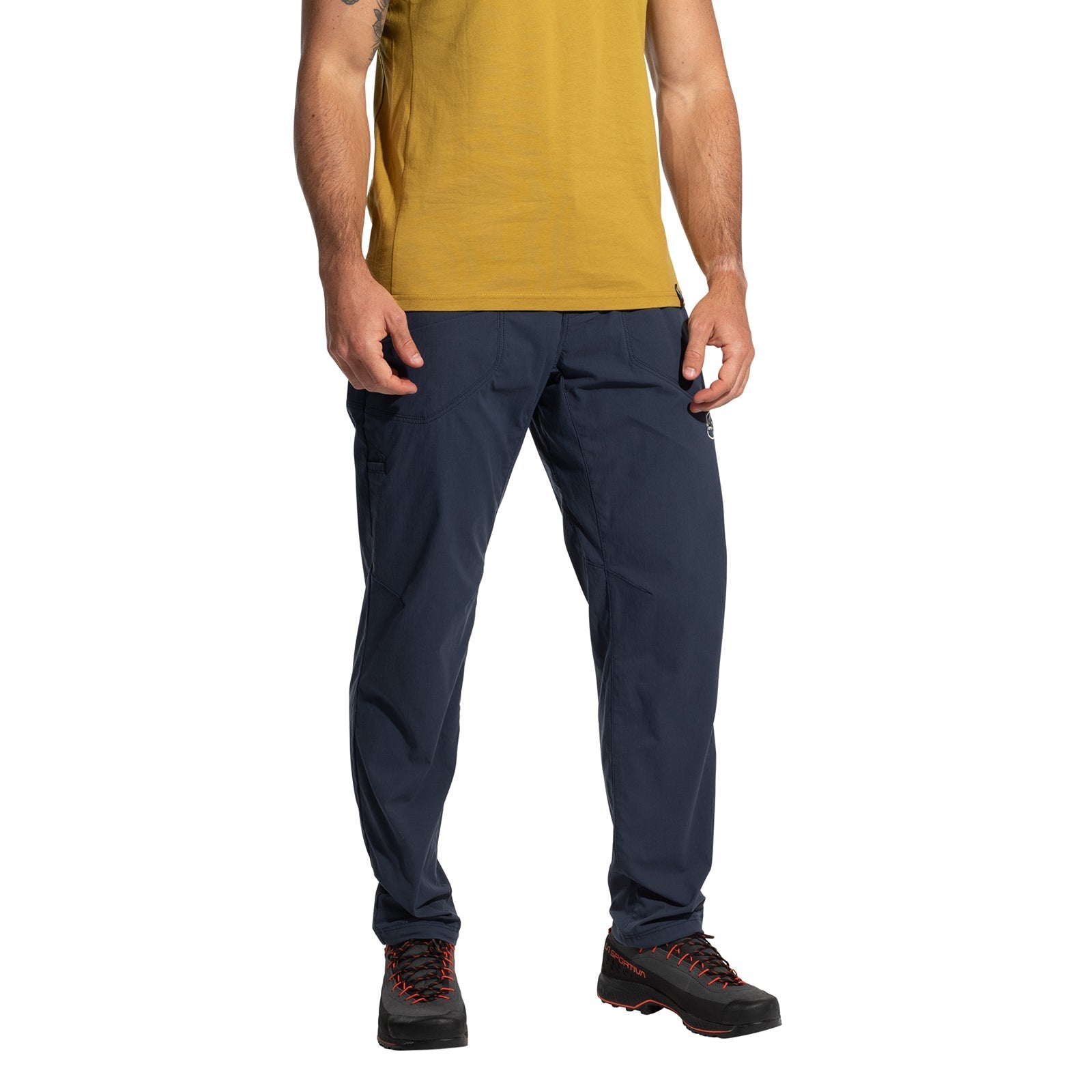 A person wearing a yellow short-sleeve shirt, La Sportiva Labyrinth Pants Men's (2025) in dark blue with an adjustable waistband, and black hiking shoes with red laces stands against a white background. The person’s head is not visible.