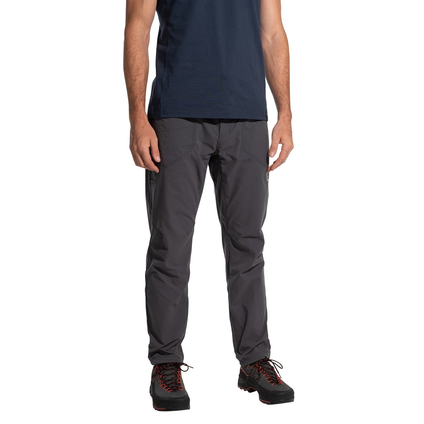 A person wearing La Sportiva Labyrinth Pants Men's (2025) in dark gray, paired with a navy t-shirt and black hiking shoes with red laces, stands against a white background; only the lower torso, legs, and feet are visible.
