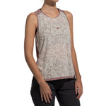 A woman wears the La Sportiva Magic Tank Women's—a sleeveless, patterned beige and mauve recycled top with an eye design on the chest—paired with dark pants, standing against a white background.