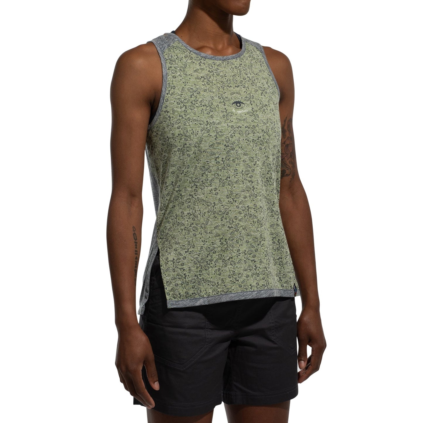 A woman wears the La Sportiva Magic Tank, a sleeveless green bamboo-patterned top with grey trim and an eye symbol on the chest, paired with black shorts, standing against a plain white background.