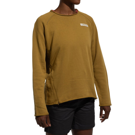 A person wears a La Sportiva Tufa Sweater Women's (2025) in mustard yellow, featuring a small chest logo, paired with black shorts, against a white background.