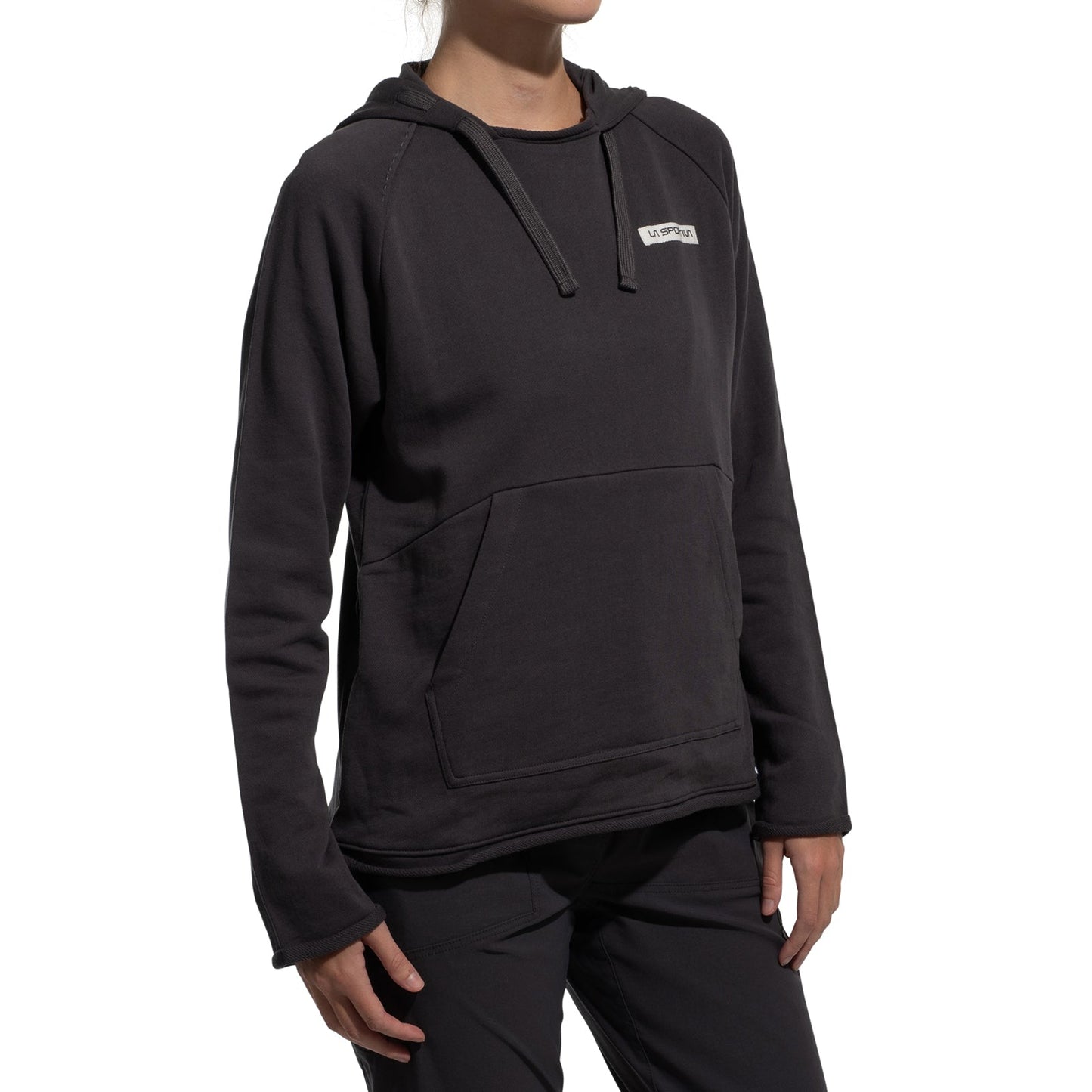A person wearing the La Sportiva Telendos Hoody Women's (2025), a dark organic cotton hoodie with a front pocket and small rectangular chest logo, stands against a plain white background.