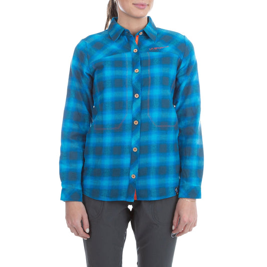 A woman wears a blue La Sportiva Rambler Flannel Shirt Women's (2024) with gray pants, standing forward with relaxed arms, ready for climbing or showcasing practical mountain wear against a plain white background.