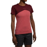 A person wearing a La Sportiva Roof T-Shirt Women's (2025) in short-sleeve maroon and pink, along with black shorts, stands against a white background. The person's head is not visible.