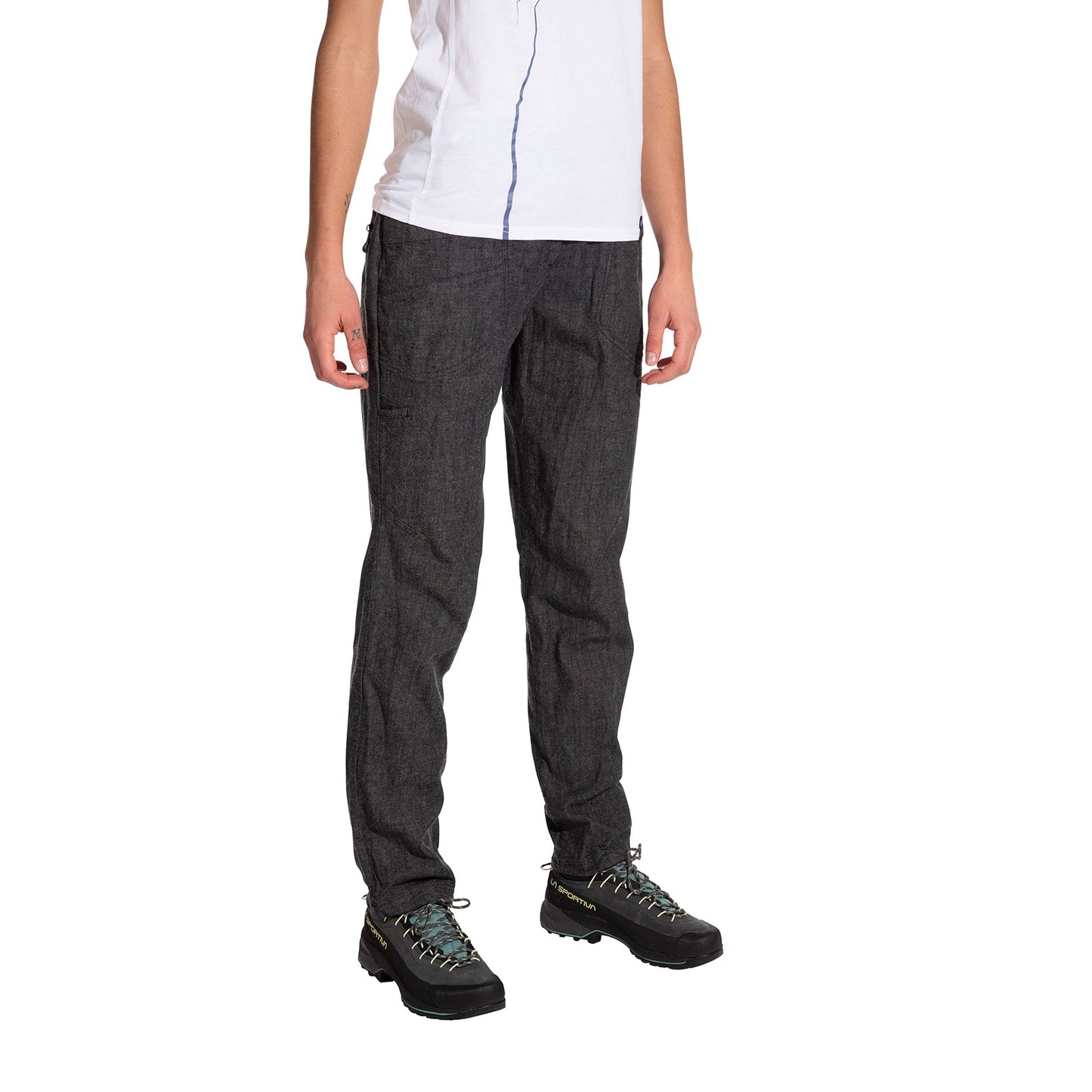 A person stands against a plain white background wearing La Sportiva Sierra Rock Pants Women's in dark gray, paired with a white short-sleeve shirt and black hiking shoes. The person's head is not visible in the image.