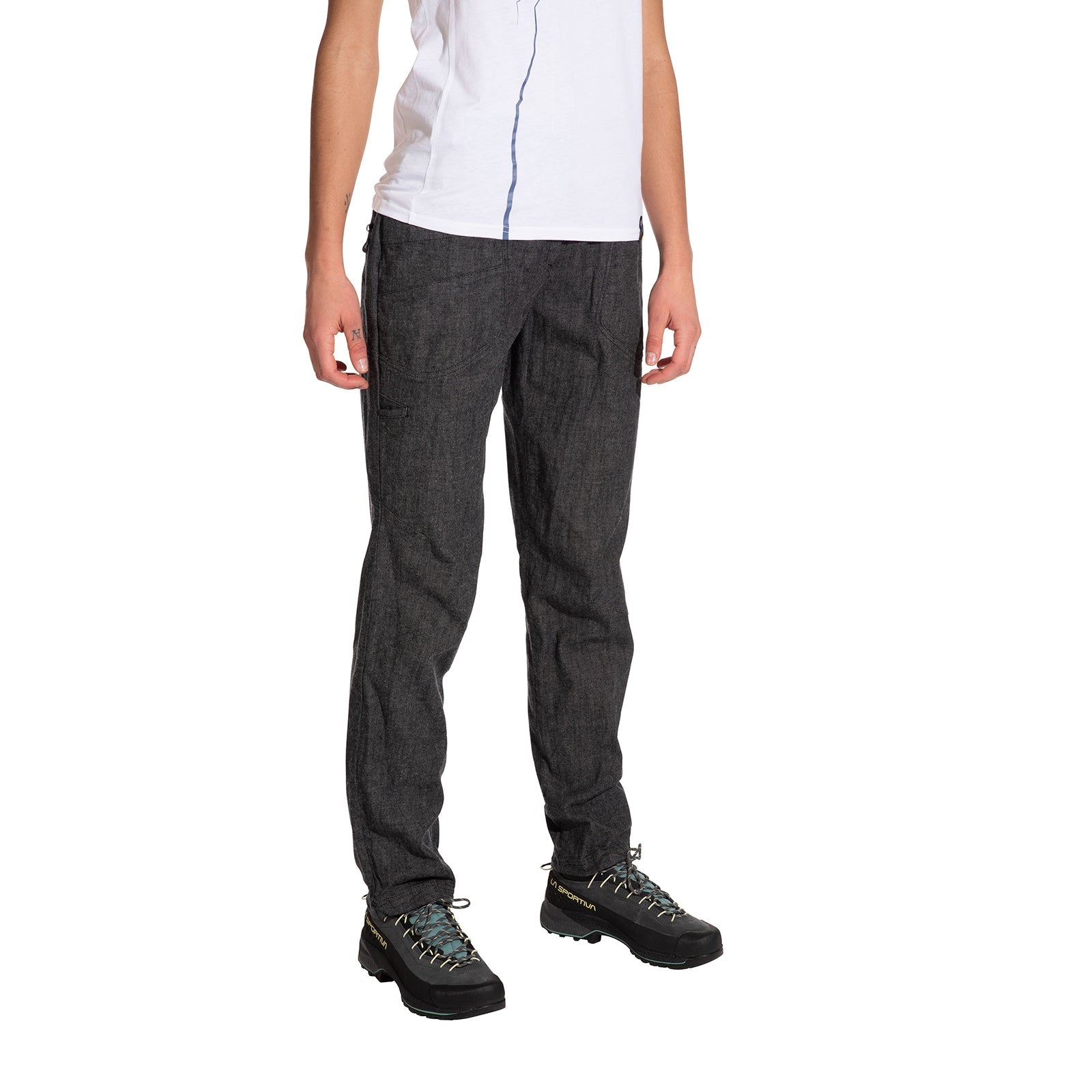 A person stands against a plain white background wearing La Sportiva Sierra Rock Pants Women's in dark gray, paired with a white short-sleeve shirt and black hiking shoes. The person's head is not visible in the image.