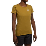 A minimalist climber wears a mustard yellow La Sportiva Circle Logo T-Shirt Women's (2025) with a small white logo on the chest and black shorts, standing against a white background.