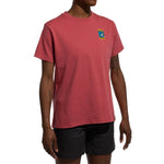 A woman wears the La Sportiva Moon Climb T-Shirt Women's (2025) in salmon pink—featuring organic cotton and a small chest graphic—with black shorts, against a plain white background.