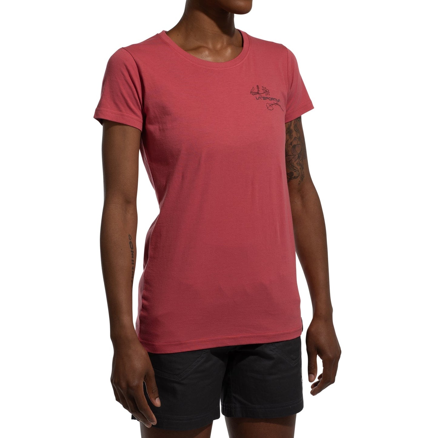 A woman wears a fitted, short-sleeve red La Sportiva Climb Flower T-Shirt Women's (2025) made from organic cotton with a small chest logo and black shorts, standing against a plain white background.