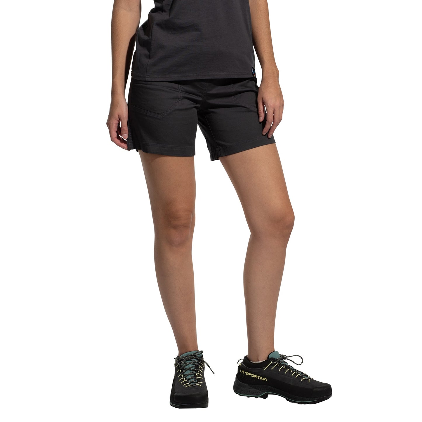 A person wears La Sportiva Roots Shorts Women's (2025) with a comfortable waistband, a black t-shirt, and black hiking shoes with teal laces. Only the lower half of their body is visible against a plain white background.