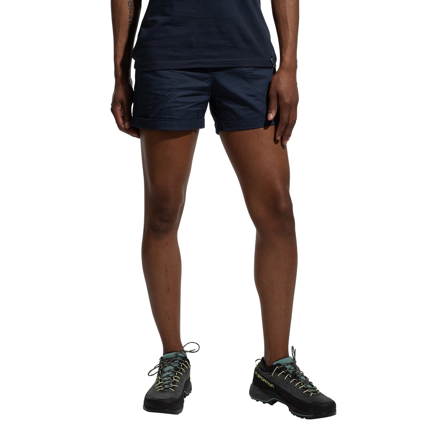 A person models La Sportiva Tundra Shorts Women's in navy blue, featuring an adjustable waistband, and black hiking shoes with light blue laces. The photo shows only their lower torso, legs, and feet against a white background.