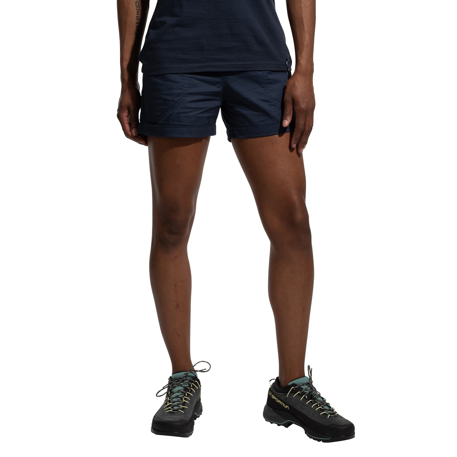 A person models La Sportiva Tundra Shorts Women's in navy blue, featuring an adjustable waistband, and black hiking shoes with light blue laces. The photo shows only their lower torso, legs, and feet against a white background.