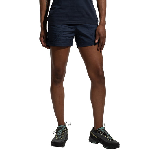 A person models La Sportiva Tundra Shorts Women's in navy blue, featuring an adjustable waistband, and black hiking shoes with light blue laces. The photo shows only their lower torso, legs, and feet against a white background.