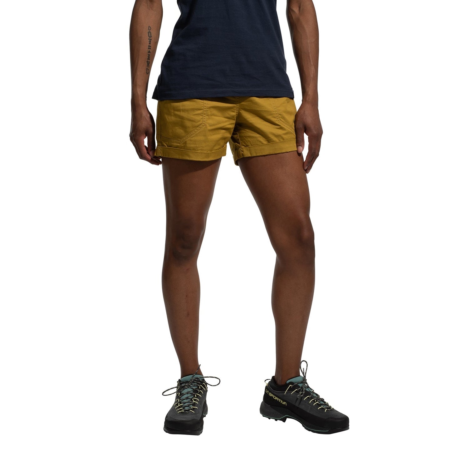 A person wearing La Sportiva Tundra Shorts Women's in mustard yellow with an adjustable waistband, a navy t-shirt, and black hiking shoes stands against a white background; only the lower torso and legs are shown.