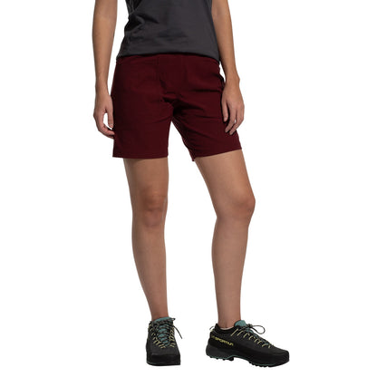 A person in a dark gray t-shirt, La Sportiva Mantra Shorts Women's (2025) in burgundy, and black hiking shoes with teal laces stands against a plain white background with arms relaxed at their sides.