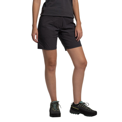 A person stands against a plain white background wearing a black t-shirt, La Sportiva Mantra Shorts Women's (2025) in dark gray made from recycled fabric, and black hiking shoes with teal laces. The person's face is not visible.