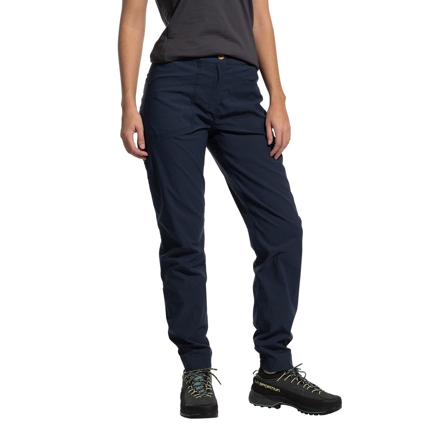 A person wears La Sportiva Mantra Pants Women's (2025) in navy blue, paired with a dark grey t-shirt and black hiking shoes, posing with one hand in their pocket against a white background. Their head is not visible.