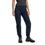 A person wears La Sportiva Mantra Pants Women's (2025) in navy blue, paired with a dark grey t-shirt and black hiking shoes, posing with one hand in their pocket against a white background. Their head is not visible.