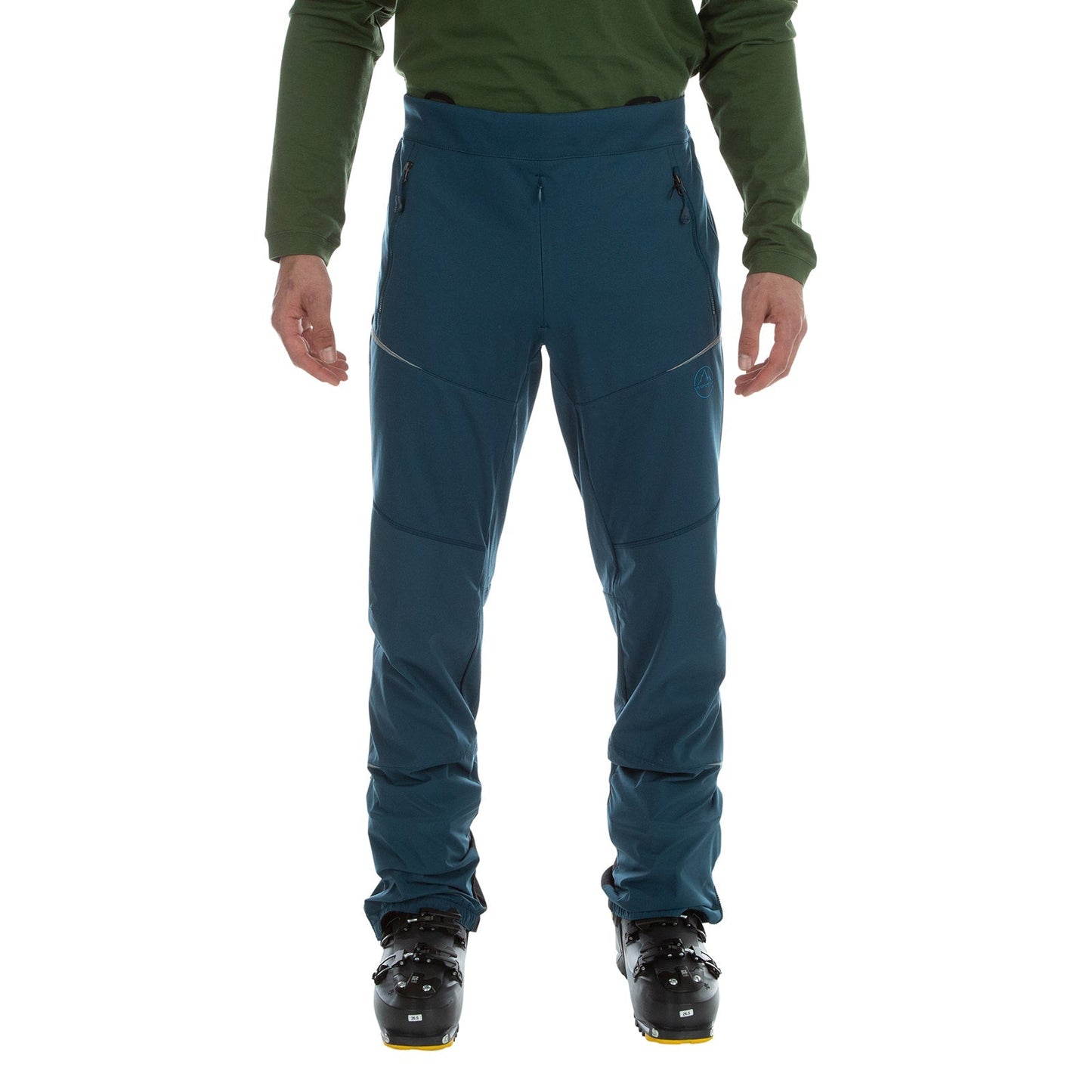 A person in a green long-sleeve shirt, La Sportiva Ikarus Pants Men's (2023), and black ski boots stands facing forward against a plain white background.