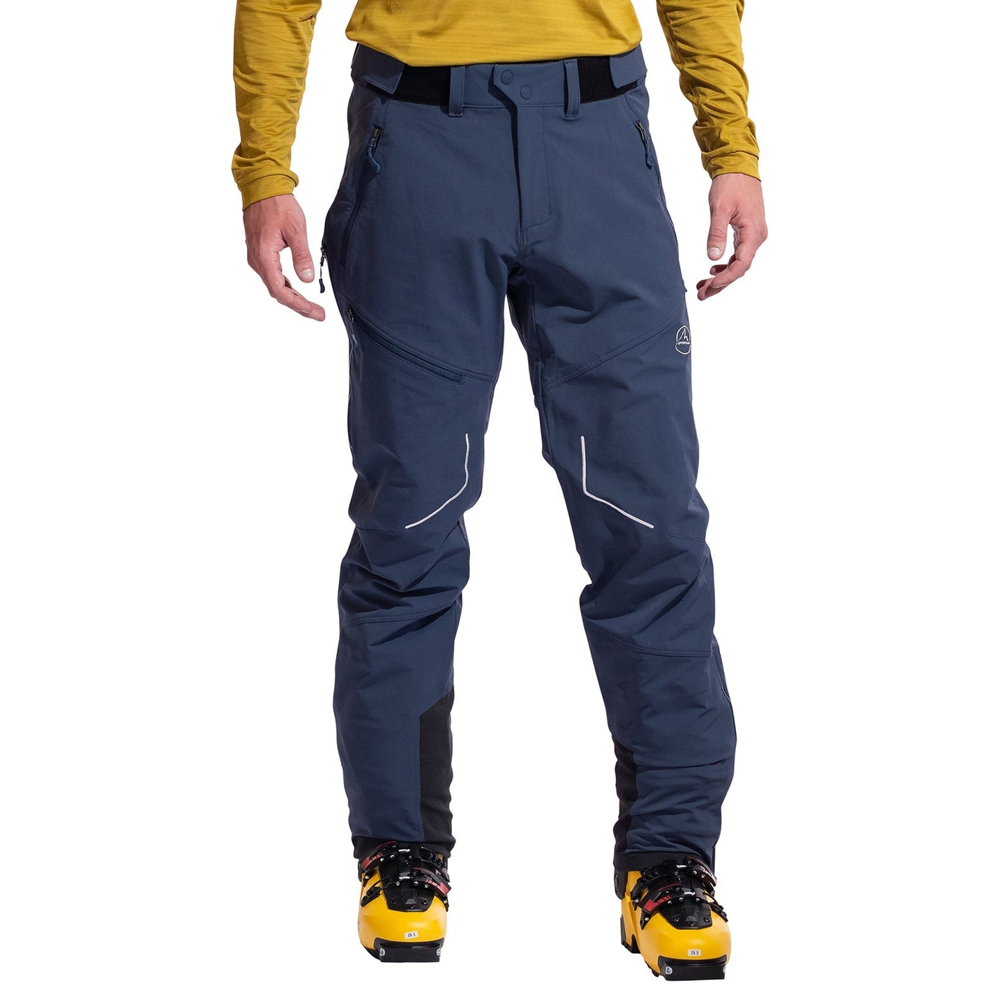 A person in a yellow long-sleeve shirt, La Sportiva Excelsior Pants Men's (dark blue with white detailing), and yellow ski boots stands facing forward against a white background.