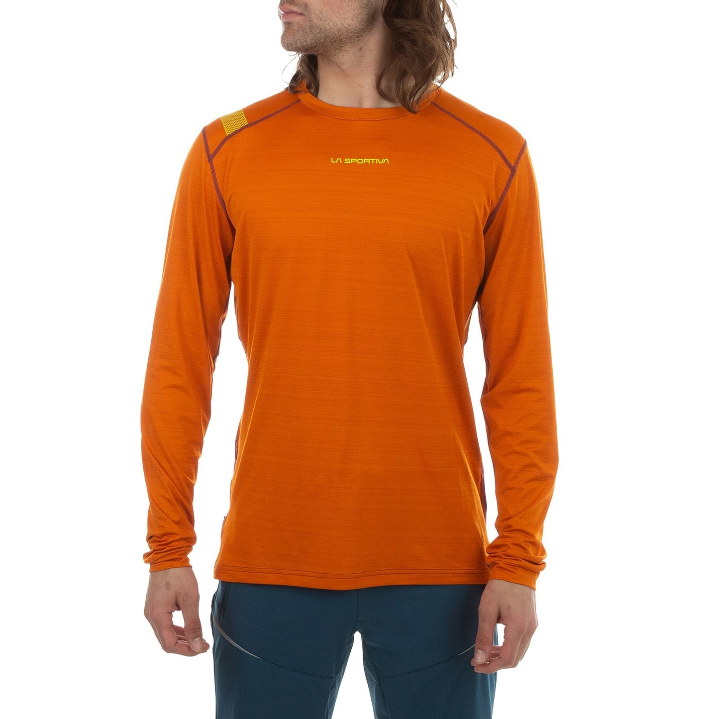 A person wears the La Sportiva Tour Long Sleeve Men's shirt in bright orange with reflective accents and logo, paired with dark blue pants, standing against a white background—perfect for winter activities.