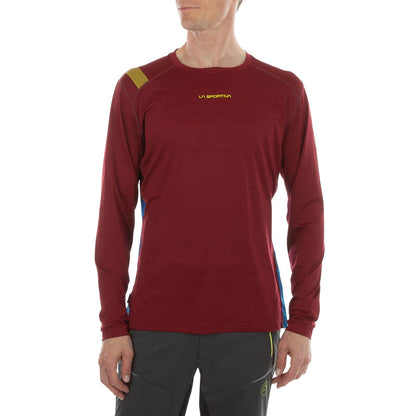 A person wears a La Sportiva Tour Long Sleeve Men's shirt in maroon with yellow logo, reflective details, and dark outdoor pants; the background is plain white.