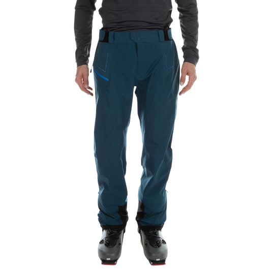 A person wearing La Sportiva Crizzle EVO Shell Pants Men's in dark blue, made from recycled materials, with a dark long-sleeve top and black ski boots, is shown from the lower torso down against a plain white background.