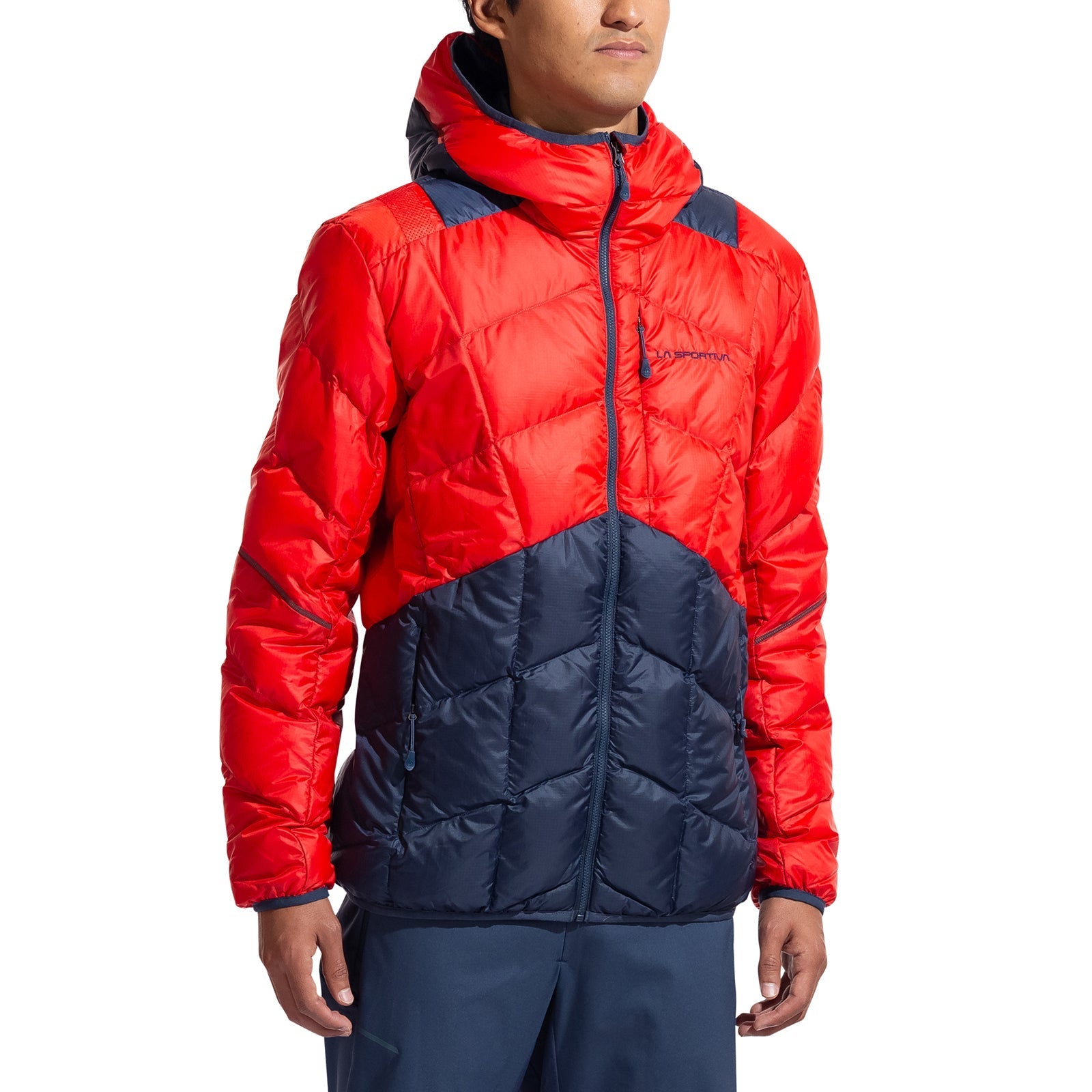 A man wears the La Sportiva Pinnacle Down Jacket—a hooded, color-blocked puffer with down insulation, bright red upper, and dark navy lower half—paired with matching navy pants, standing against a plain white background.