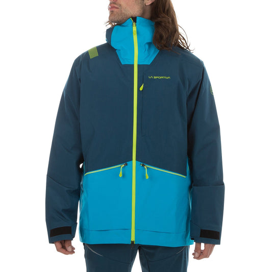 A person wears the La Sportiva Chaser EVO Shell Jacket Men's—a blue and teal ski touring shell with a high collar, hood, underarm vents, and neon yellow zippers—standing against a plain white background.
