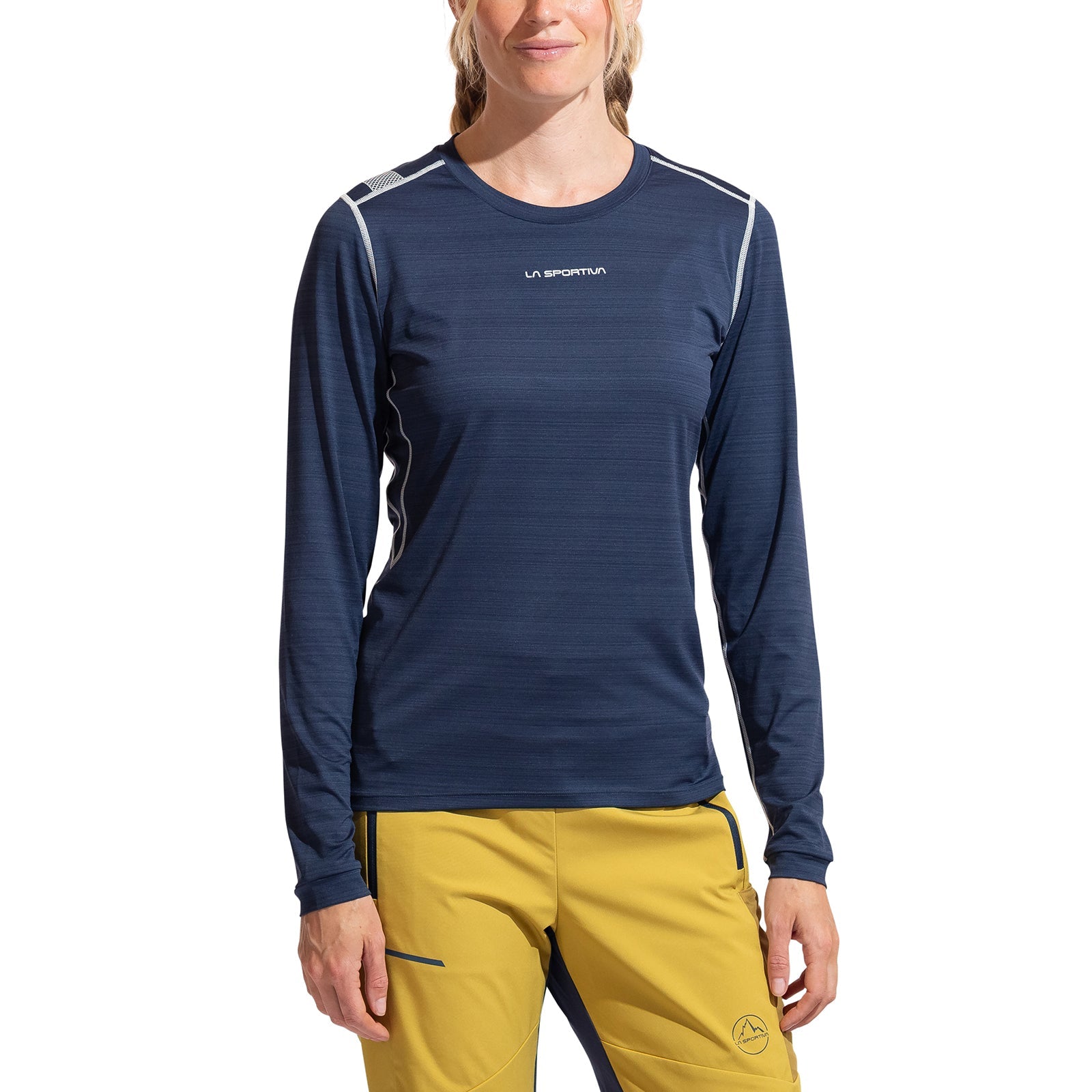 A person wears the La Sportiva Tour Long Sleeve Women's shirt in dark blue with anti-odor tech and yellow pants, standing against a white background. The La Sportiva logo is visible. Their face is partially visible with a slight smile.