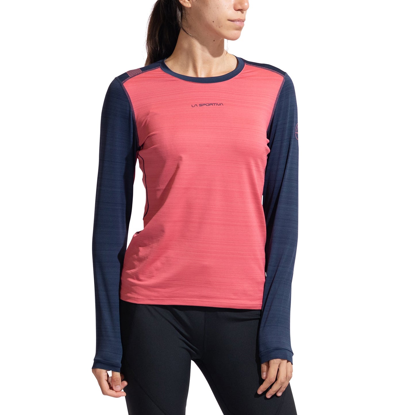 A woman models the La Sportiva Tour Long Sleeve Women's shirt, featuring pink with navy blue sleeves and a women’s-specific fit, paired with black leggings, against a plain white background.