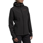 A person wearing the La Sportiva Descender Storm Jacket Women's (2025), a black softshell with fleece interior, side pockets, and front zipper, stands against a white background. The La Sportiva logo is on the chest; their face is partly out of frame.