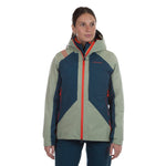 A woman with dark hair pulled back faces forward in the La Sportiva Crizzle EVO Shell Jacket Women's, featuring a color-blocked design in green and blue with orange zippers and a hood, as she gazes slightly to the side.
