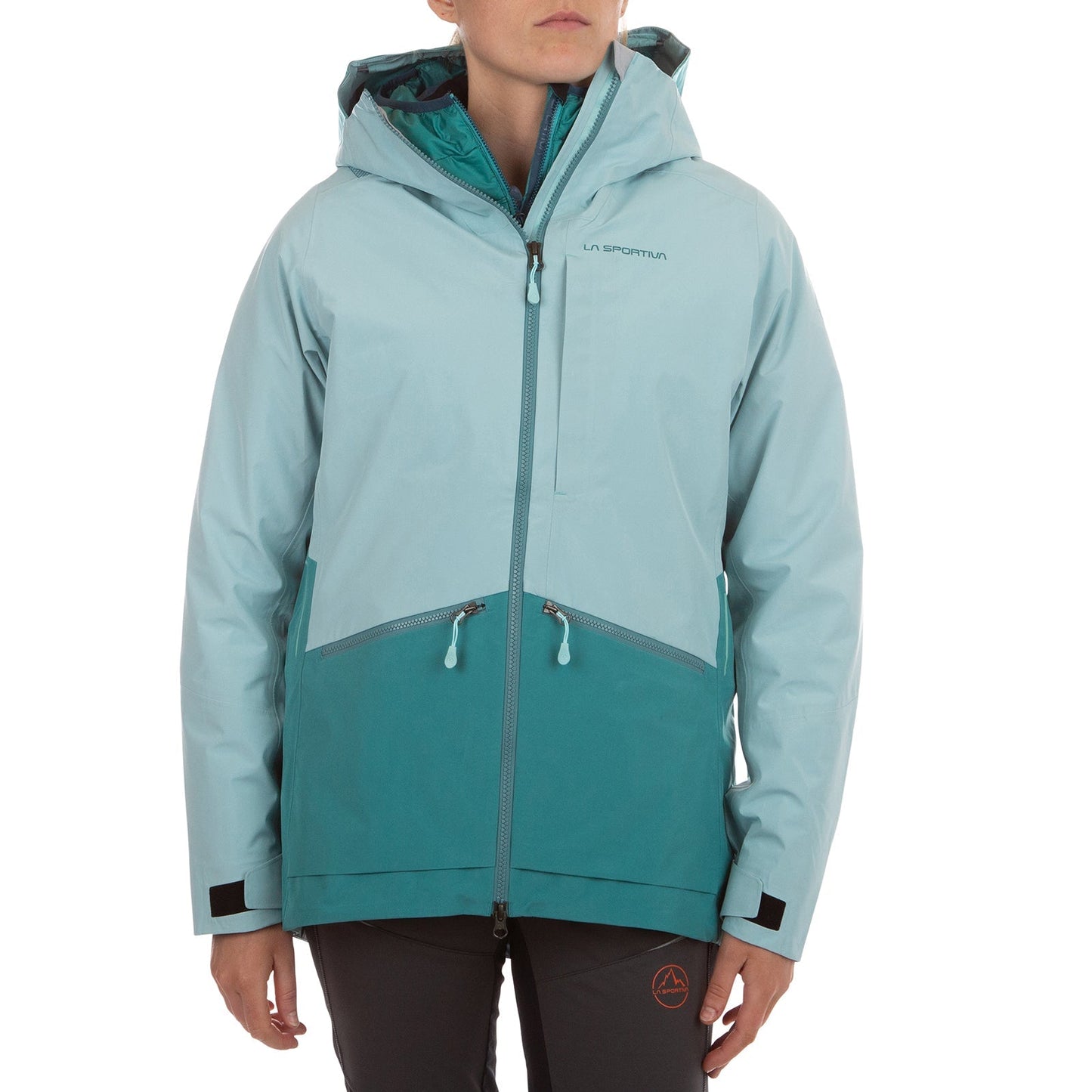 A person wears the La Sportiva Chaser EVO Shell Jacket Women's in light blue and teal with black zippers, pockets, reflective details, and chest branding; paired with dark pants. The face is partially visible.