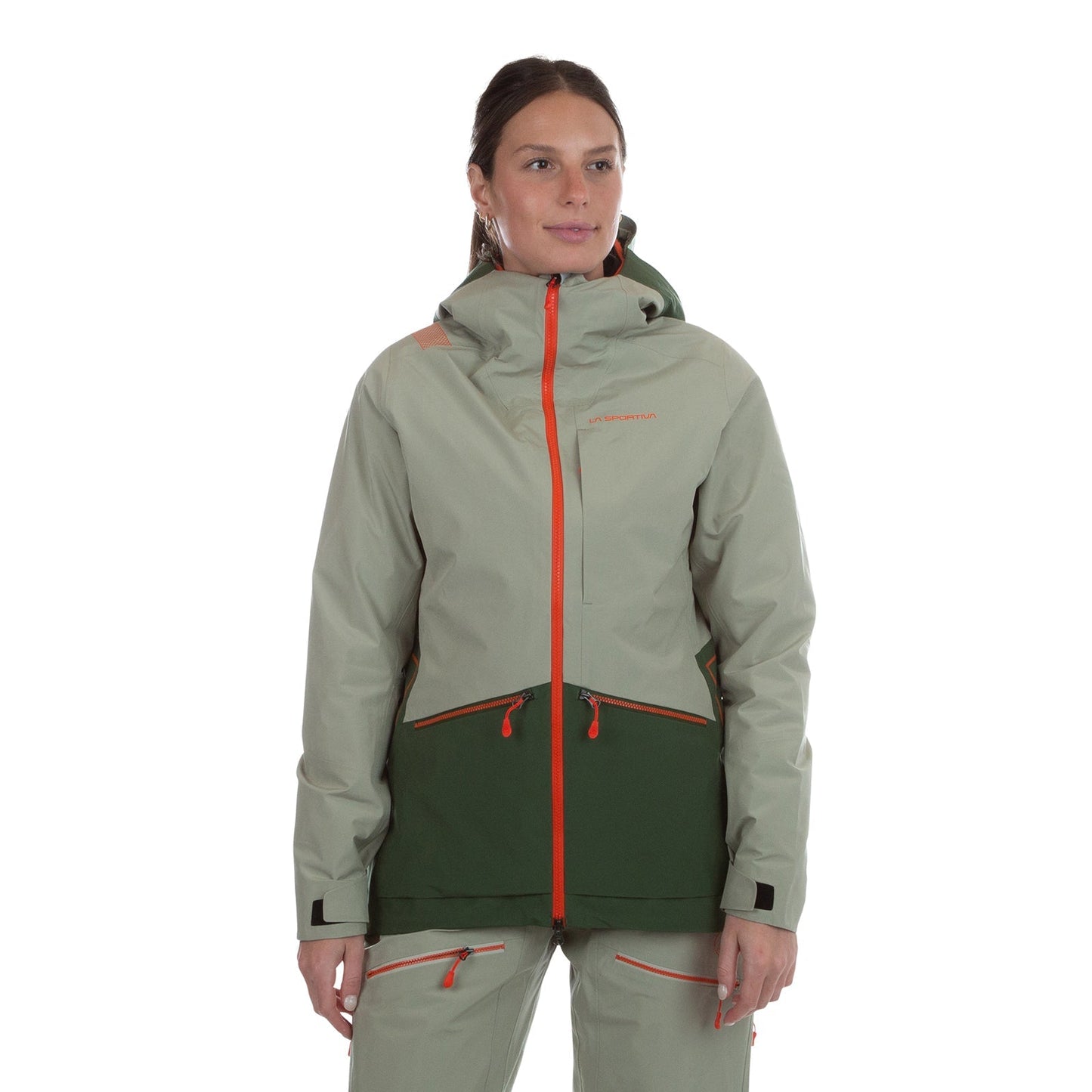 A woman with brown hair pulled back stands against a white background, wearing the La Sportiva Chaser EVO Shell Jacket Women's in light gray and dark green with orange zippers, reflective details, and underarm ventilation. She looks slightly to the side.
