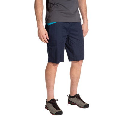 A person stands against a white background wearing La Sportiva Bleauser Shorts Men's in navy with a gusseted crotch, a gray T-shirt, and gray hiking shoes with black and red accents. The person's face is not visible.
