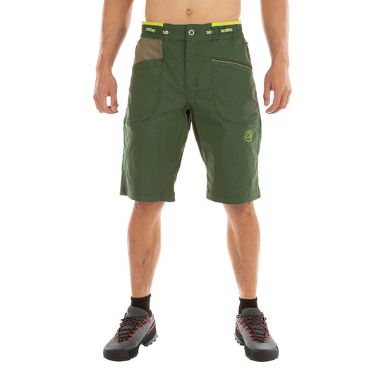 A man in La Sportiva Belay Shorts – green, knee-length, eco-friendly with zippered pockets and a yellow-accented adjustable waistband – pairs them with black hiking shoes featuring orange laces, against a white background.